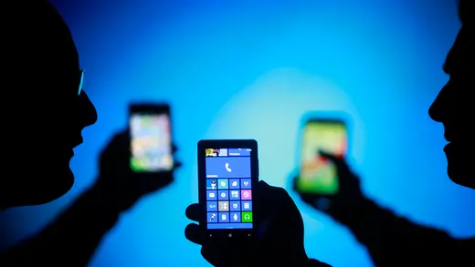 Men are silhouetted against a blue screen as they hold up their smartphones.